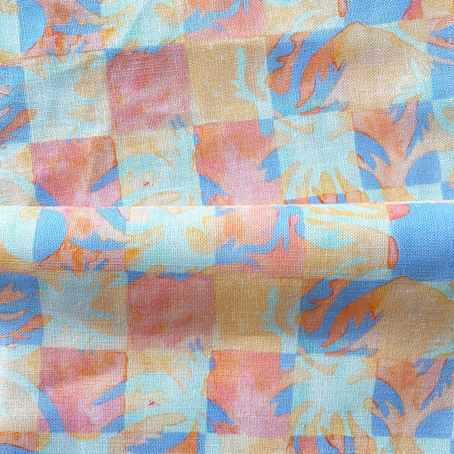 Draped fabric in a painterly tropical checkerboard design in blue, coral and orange. 