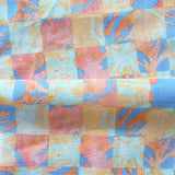 Draped fabric in a painterly tropical checkerboard design in blue, coral and orange. 