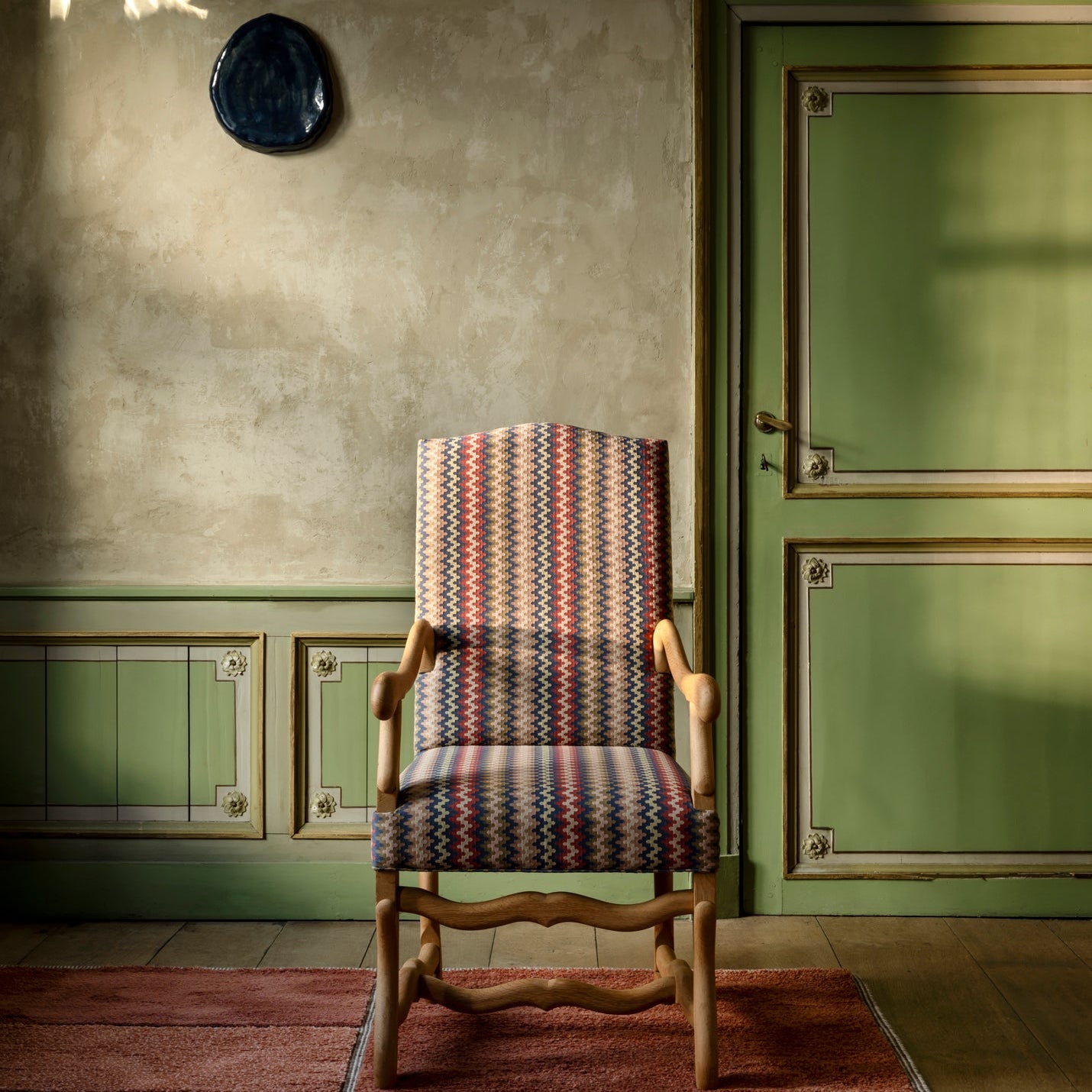Decorative chair with patterned seat in a room with green walls and a door.