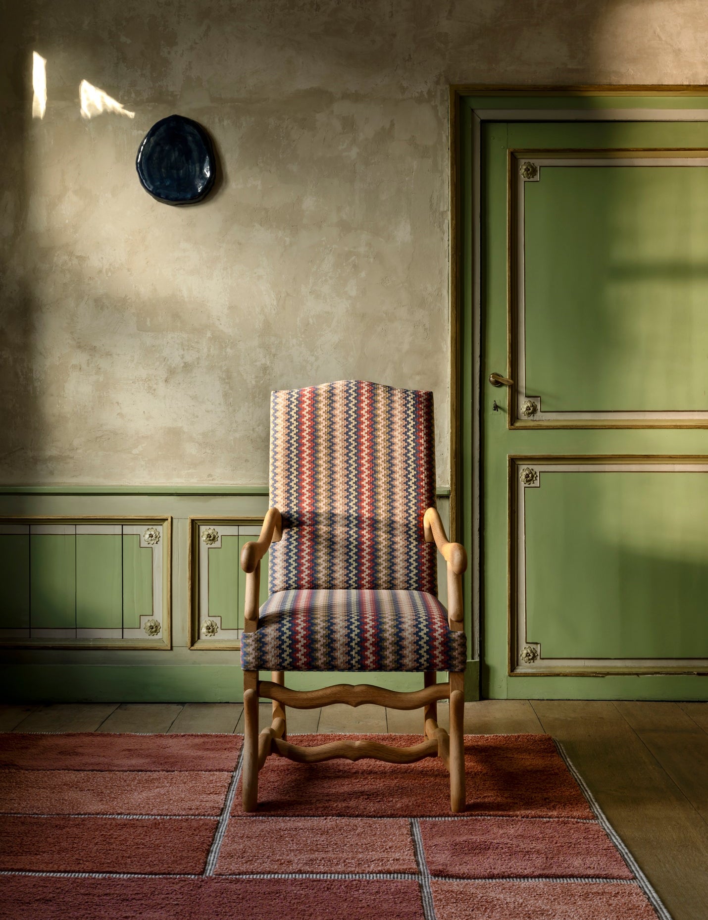 Decorative chair with patterned seat in a room with green walls and a door.