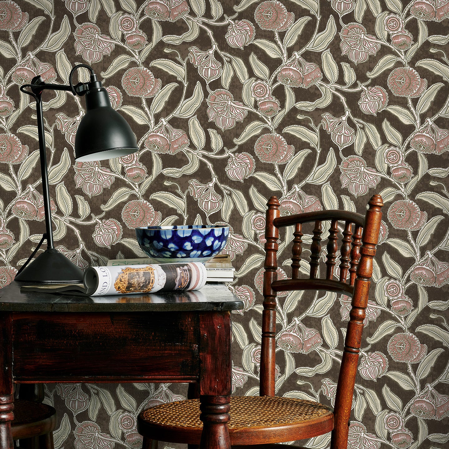 Room interior with a wooden table, chair, and lamp against a brown and pink floral-patterned wall.
