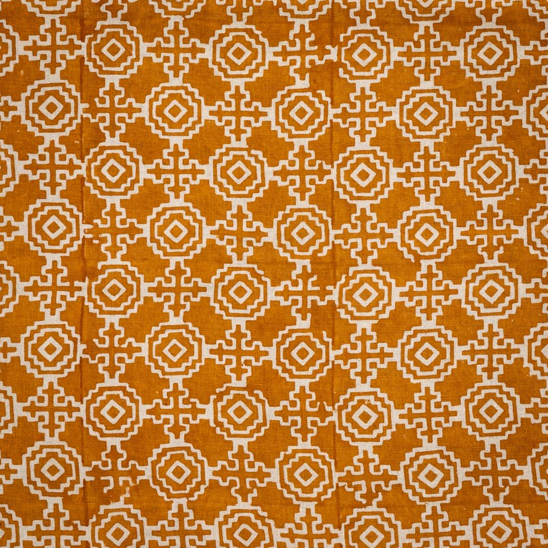 Detail of fabric in a repeating geometric print in cream on an ochre field.