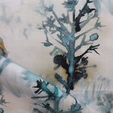 Detail of draped fabric yardage in a watercolor tree print in shades of turquoise, gray and gold on a cream field.