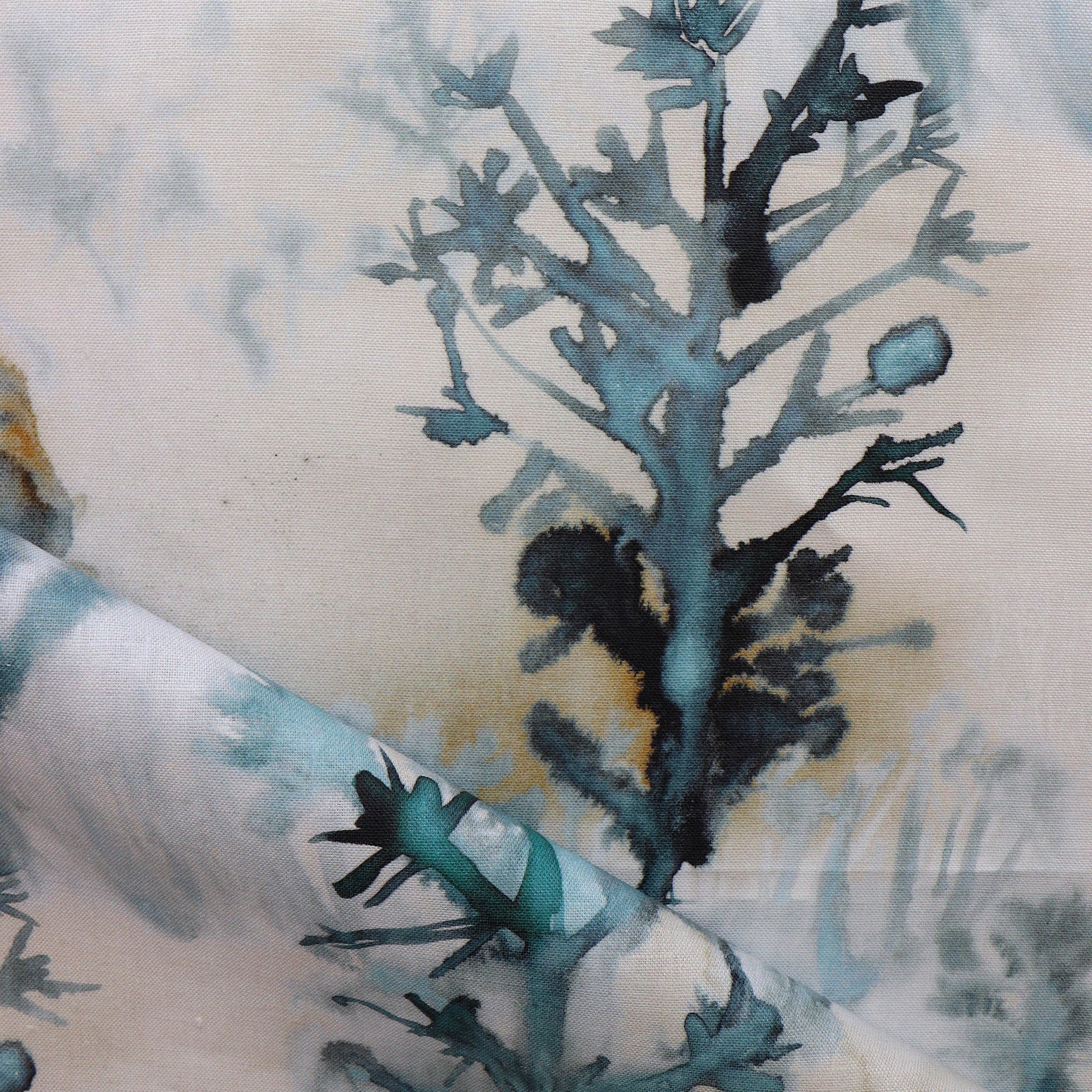 Detail of draped fabric yardage in a watercolor tree print in shades of turquoise, gray and gold on a cream field.