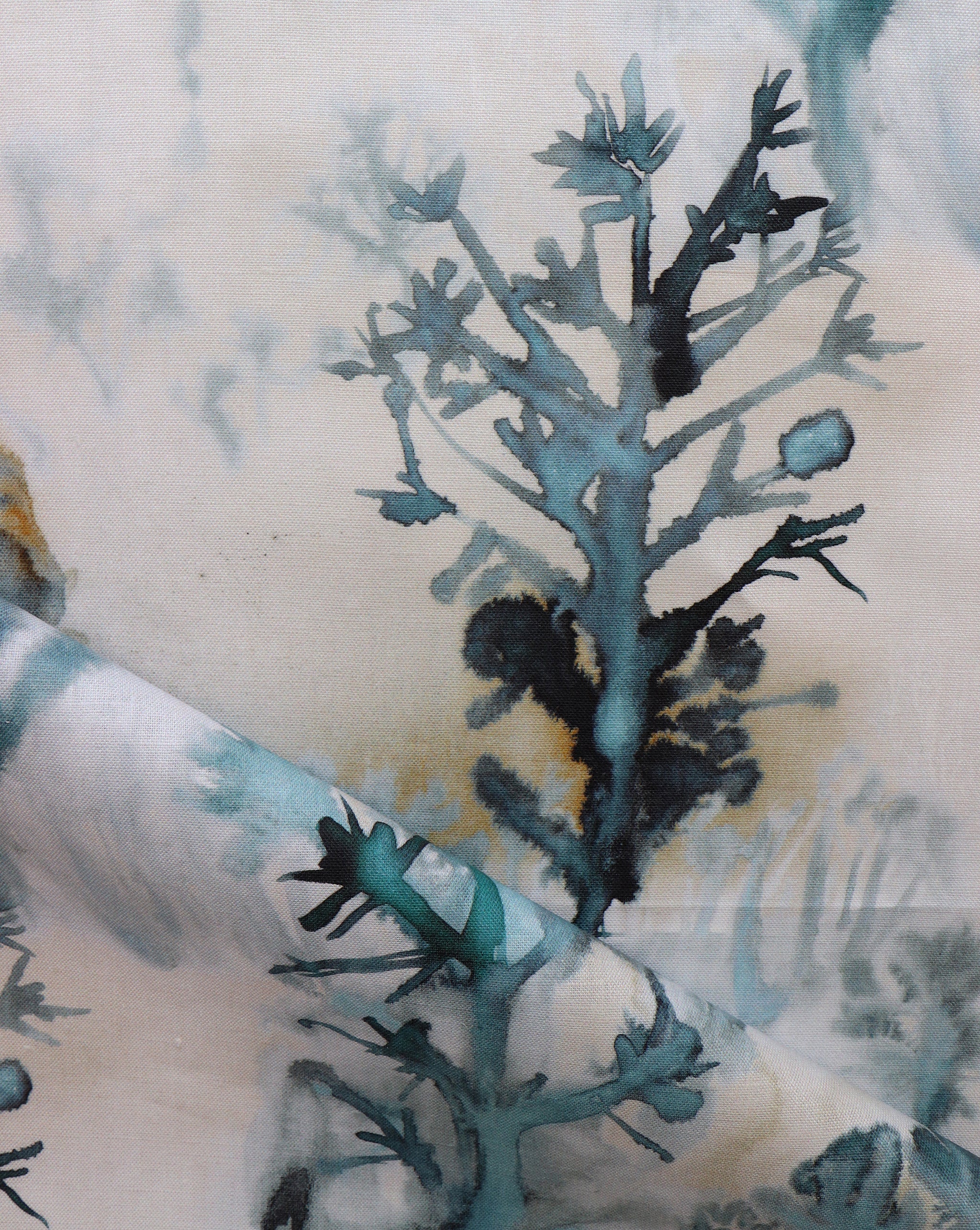 Detail of draped fabric yardage in a watercolor tree print in shades of turquoise, gray and gold on a cream field.