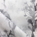 Detail of draped fabric yardage in a watercolor tree print in shades of gray and black on a white field.