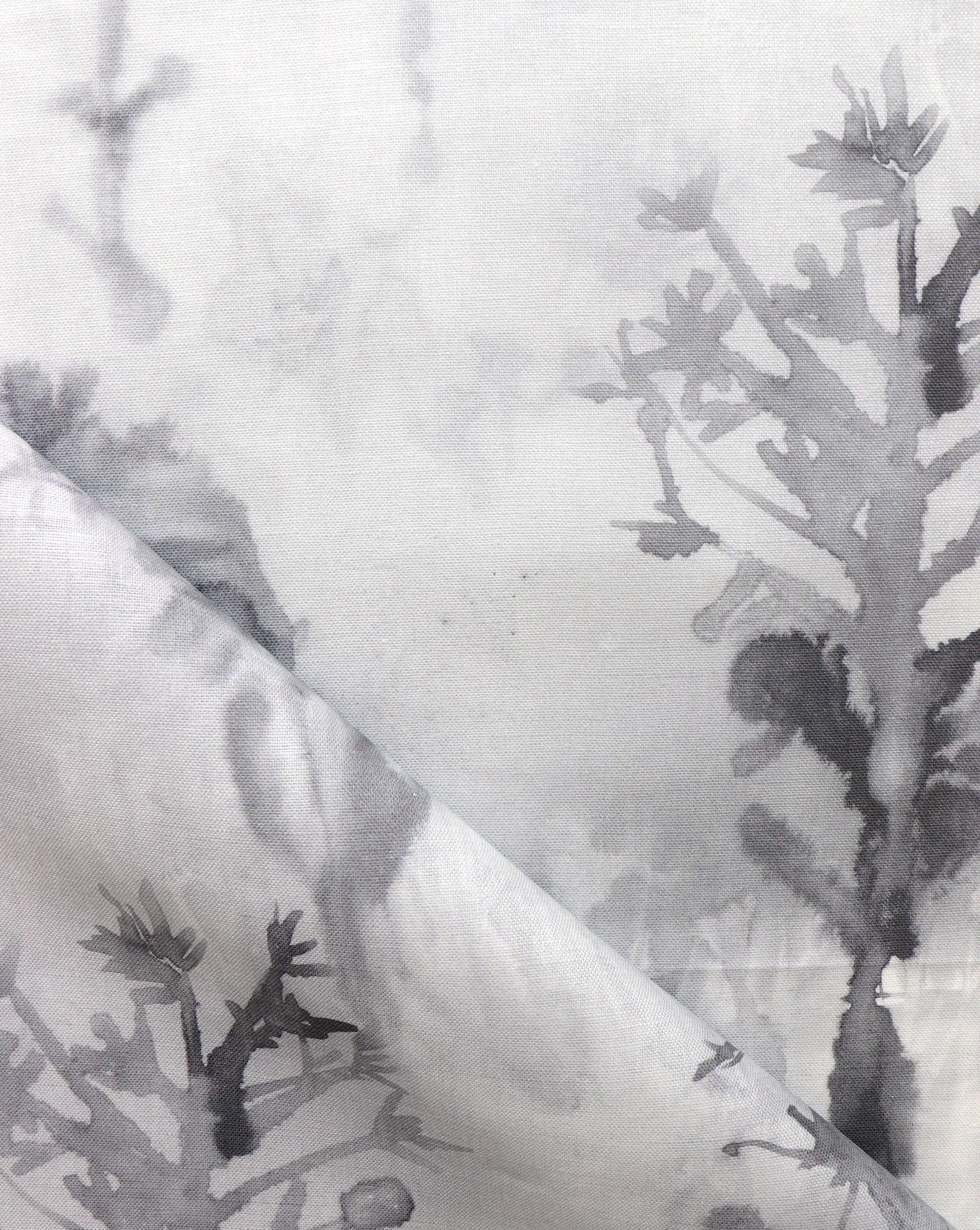 Detail of draped fabric yardage in a watercolor tree print in shades of gray and black on a white field.