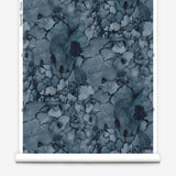 Partially unrolled wallpaper yardage in a watercolor textural print in shades of blue, navy and black.