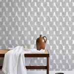 A bench with a towel and clay vases stands in front of a wall papered in an abstract scalloped print in gray and white.