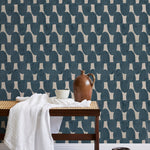 A bench with a towel and clay vases stands in front of a wall papered in an abstract scalloped print in navy and greige.