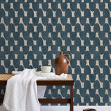A bench with a towel and clay vases stands in front of a wall papered in an abstract scalloped print in navy and greige.
