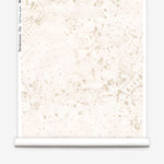 Partially unrolled wallpaper yardage in a painterly bandana print in beige on a cream field.
