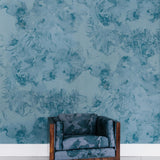 An upholstered armchair stands in front of a wall papered in a painterly floral print in shades of navy and yellow on a blue field.