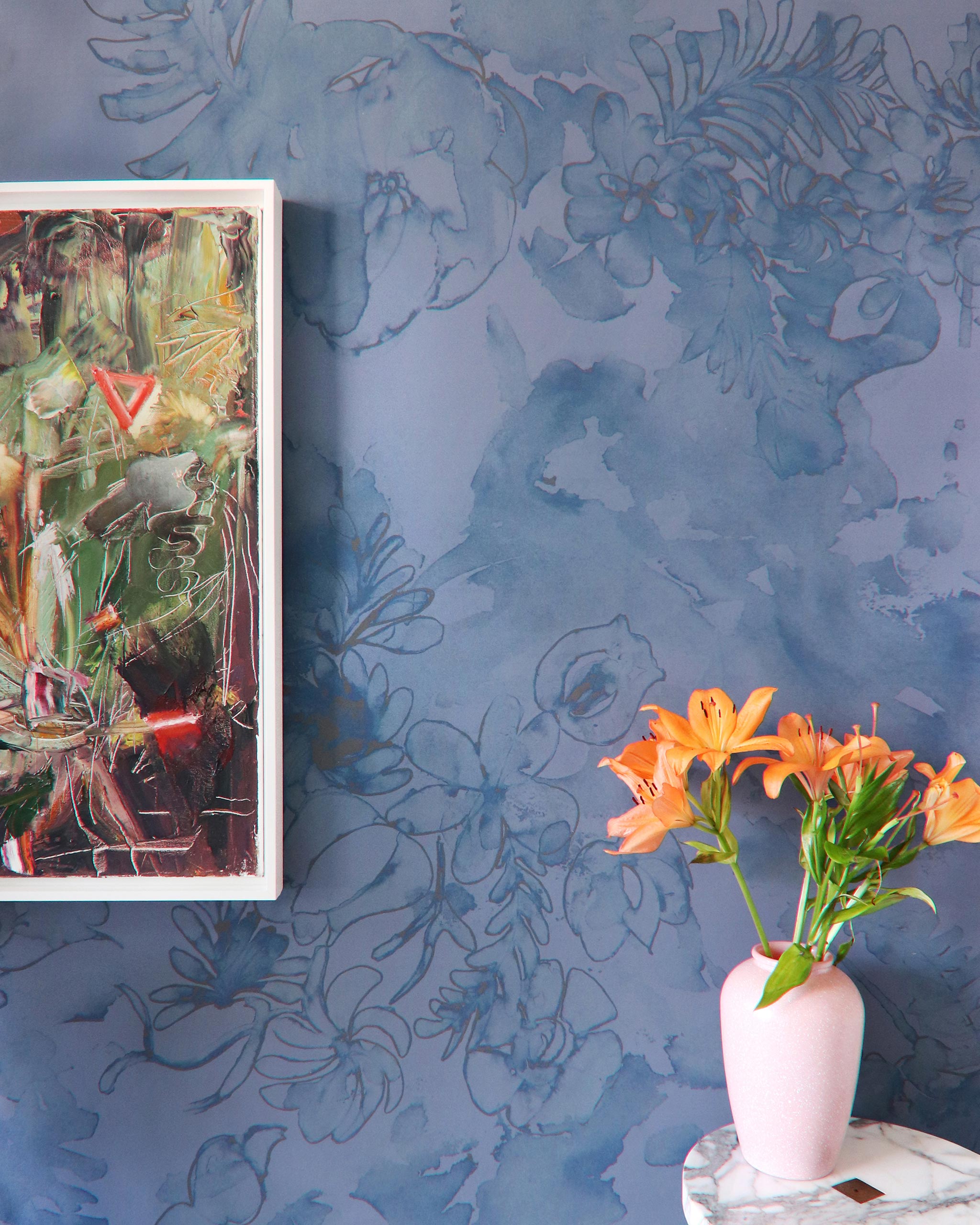 A vase of flowers and painting stand in front of a wall papered in a painterly floral print in navy, tan and blue.