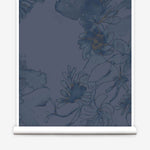 Partially unrolled wallpaper yardage in a painterly floral print in shades of navy and tan on a blue field.