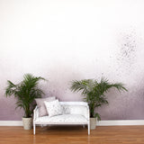 A sofa and potted plants stands in an abstract ombré paint splatter print in shades of purple, gray and white.