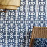 A lamp and statement chair stand in front of a wall papered in a painterly ikat print in navy and white.
