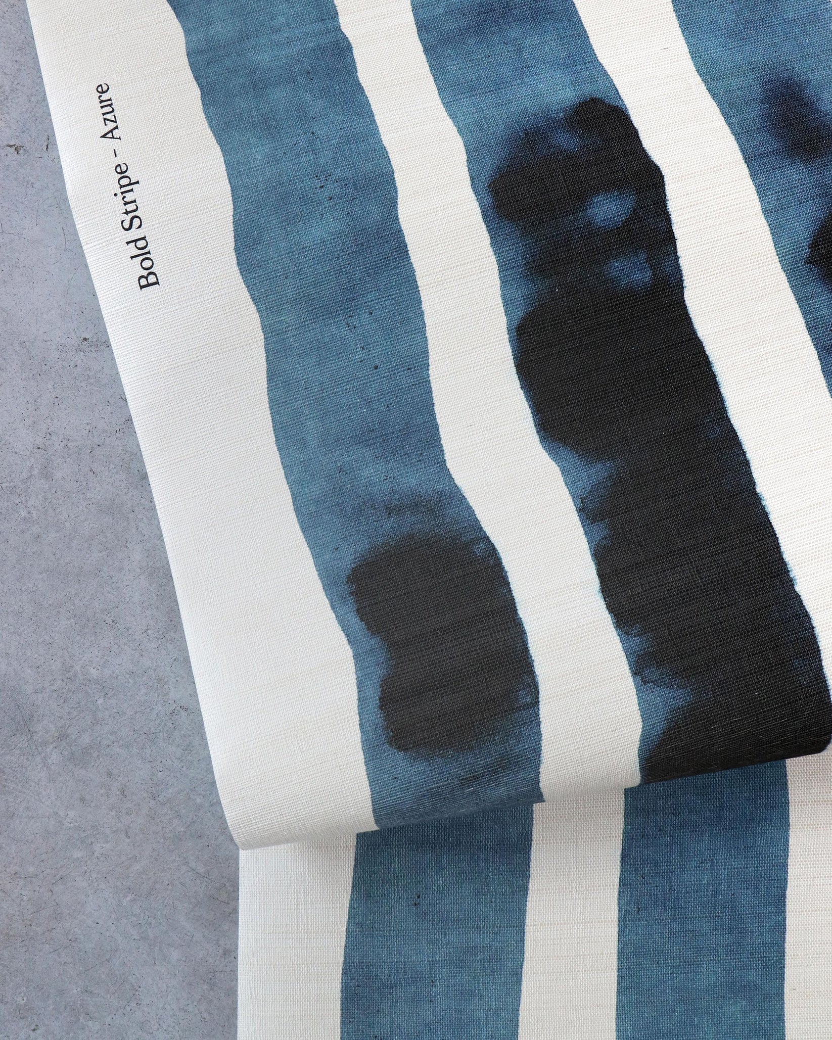 Draped crasscloth wallpaperwith bold watercolor stripes in inky blue and white on a concrete surface. 