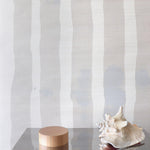 Decorative wood and steel table with conch shell against grey and cream striped grasscloth wallpaper. 