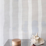Decorative wood and steel table with conch shell against grey and cream striped grasscloth wallpaper. 