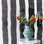 Ceramic vase on a marble table against bold black and white painted stripe wallpaper. 