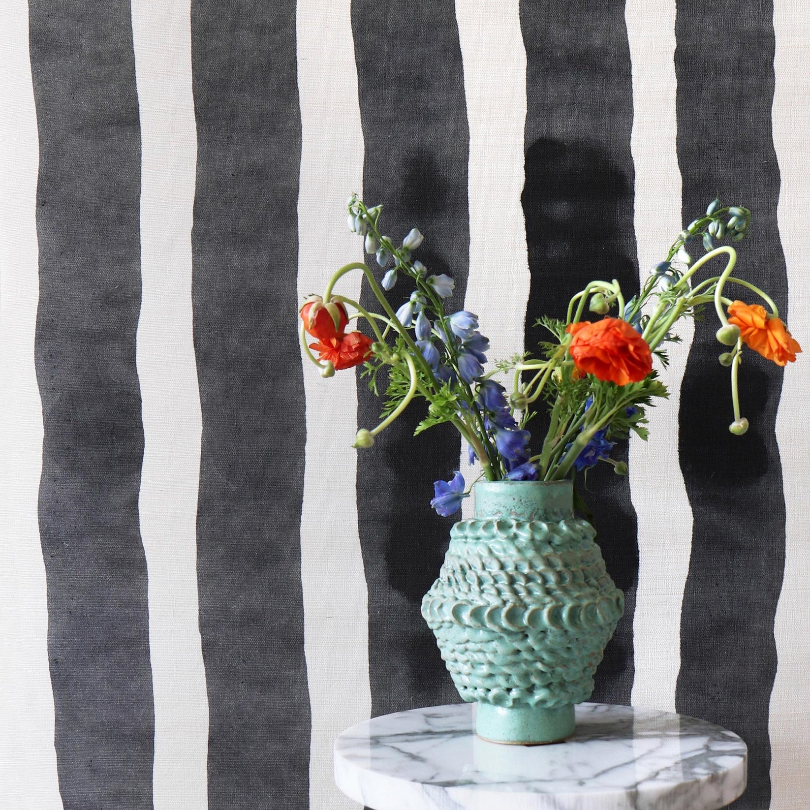 Ceramic vase on a marble table against bold black and white painted stripe wallpaper. 