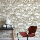 A modernist armchair stands in front of a wall papered in a painterly palm tree print in shades of gray, gold and white.