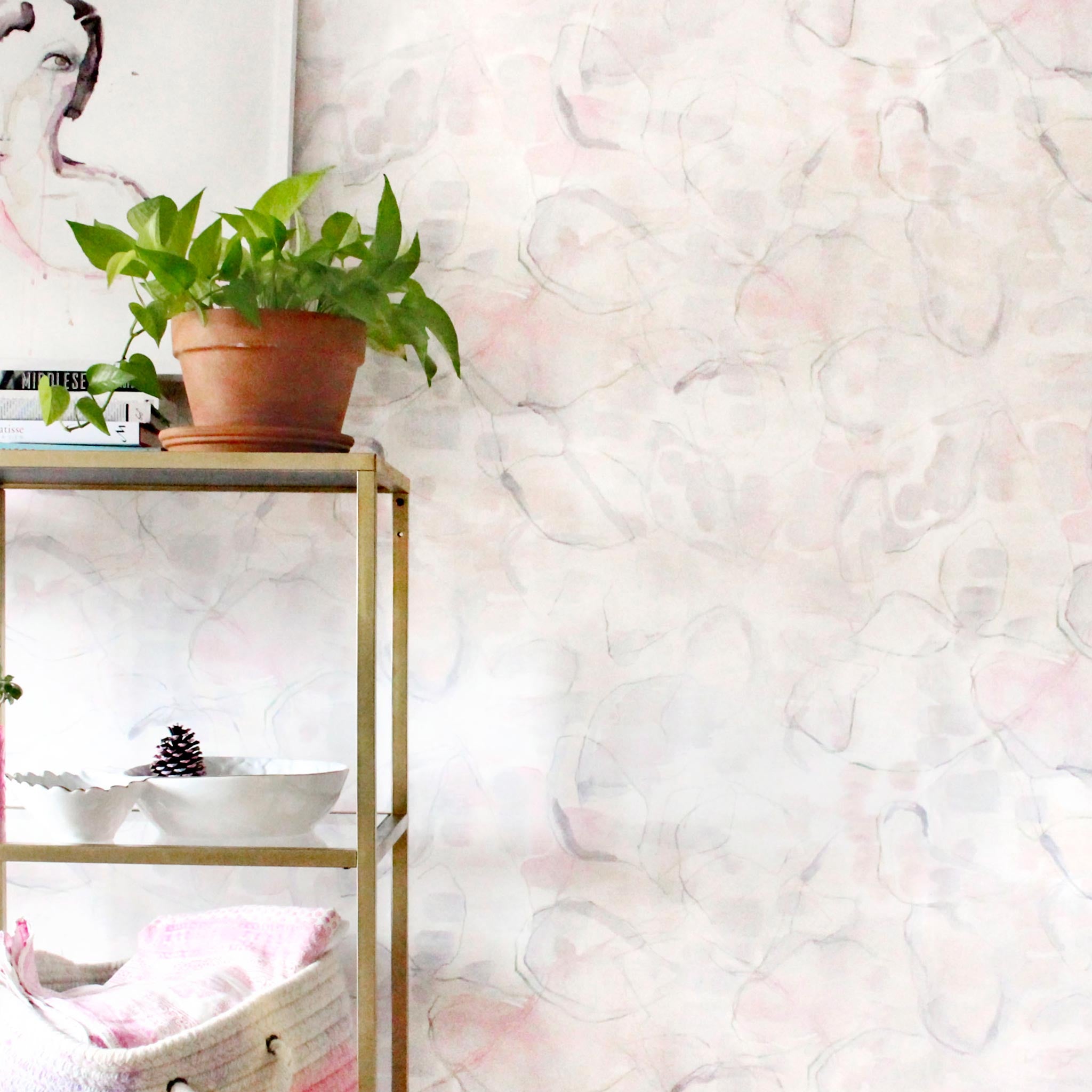 An end table with knick knacks stands in front of a wall papered in a watercolor painterly print in pastel, green and cream.