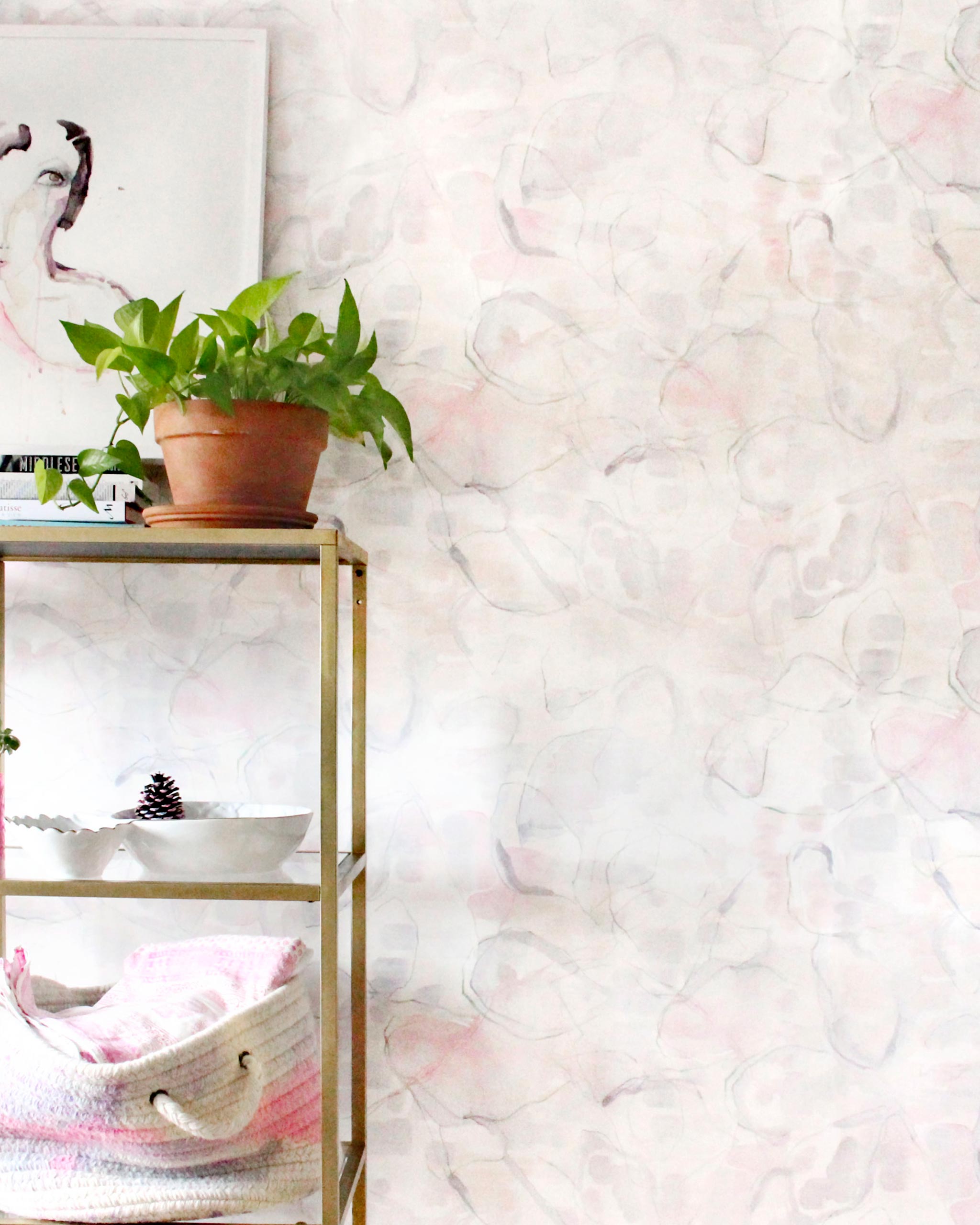 An end table with knick knacks stands in front of a wall papered in a watercolor painterly print in pastel, green and cream.