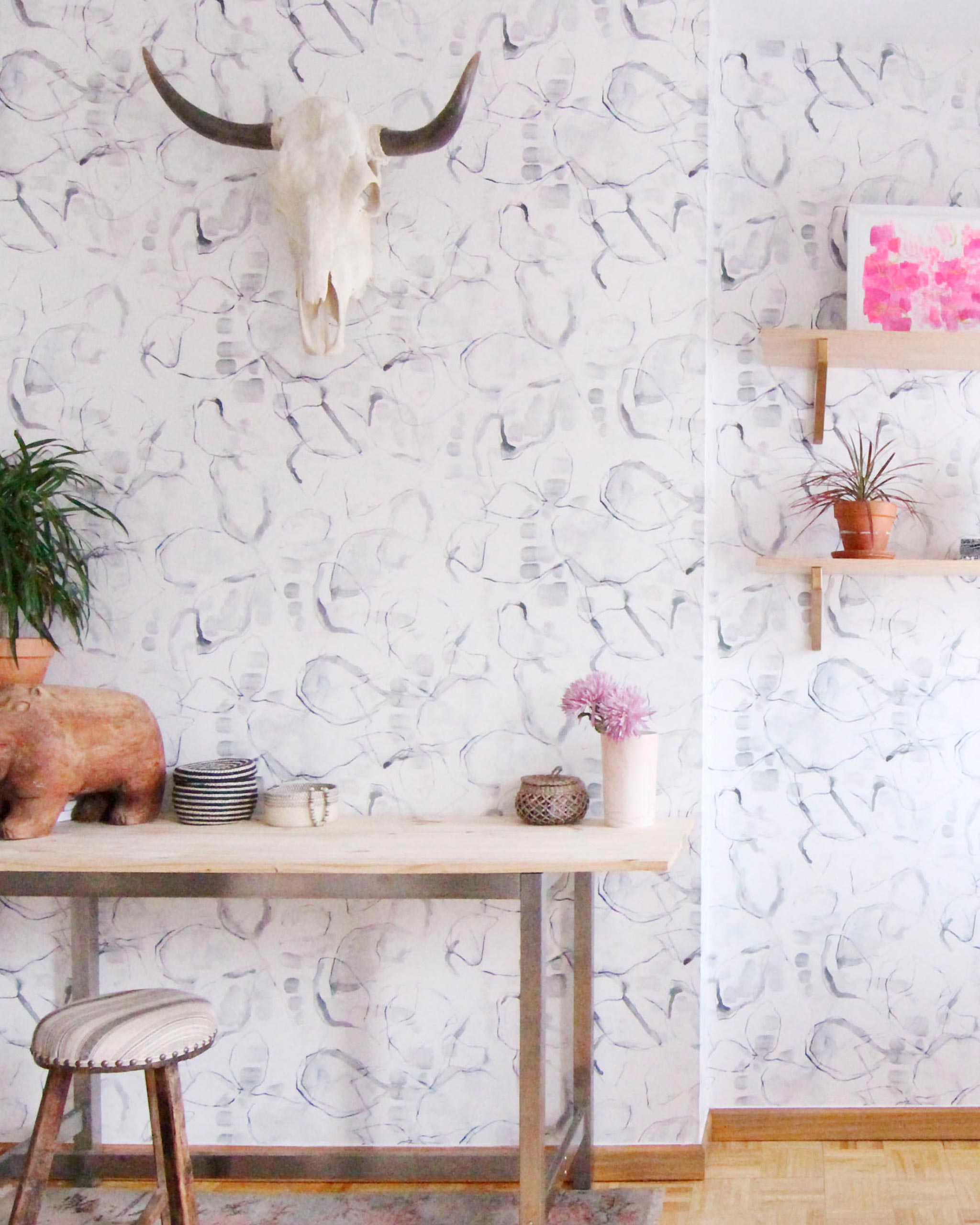 A maximalist living space with walls papered in a watercolor painterly print in shades of gray, purple and cream.
