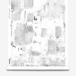 Partially unrolled wallpaper yardage in a watercolor textural print in shades of gray on a white field.