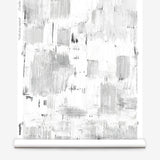 Partially unrolled wallpaper yardage in a watercolor textural print in shades of gray on a white field.