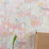 A chair and plant stand in front of a wall papered in a watercolor textural print in shades of pink, green, yellow and white.