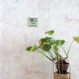 A potted plant on a stand in front of a wall papered in a watercolor textural print in shades of pink, cream and tan.