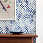 A modernist living tableau with a wall papered in a painterly chess board print in shades of blue, navy and white.