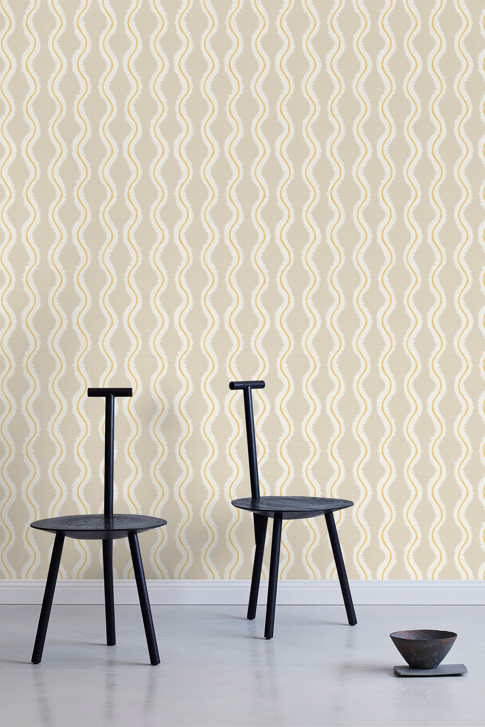 Two minimalist black chairs stand in front of a wall papered in a playful curvy stripe print in white, yellow and beige.