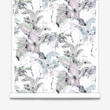 Partially unrolled wallpaper yardage in a painterly palm tree print in shades of gray, pink and green on a white field.