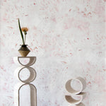 Modernist end tables stand in front of a wall papered in a watercolor painted print in shades of pink, red and white.