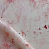 Detail of fabric in a watercolor painterly print in pink and red on a cream field.