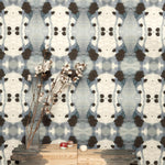 A modernist end table with flowers stands in front of a wall papered in a watercolor ink blot print in charcoal, gray and tan.