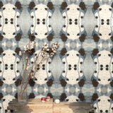 A modernist end table with flowers stands in front of a wall papered in a watercolor ink blot print in charcoal, gray and tan.