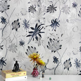 A cluttered end table stands in front of a wall papered in a playful leaf and snake print in gray, navy and cream.