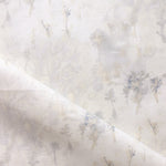 Detail of fabric in a painterly tree print in gray and tan on a white field.