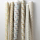 A group of fabric rolls leaned against a wall, all in different colorways of the same geometric stripe print.