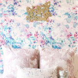 A pink couch stands in front of a wall papered in a watercolor paint blotch print in pink, green, turquoise and white.