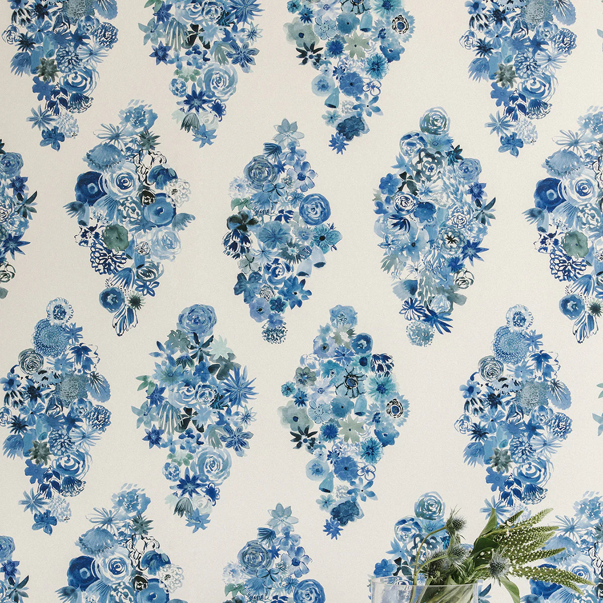 A vase of flowers stands in front of a wall papered in a painterly floral print in shades of blue and navy on a cream field.