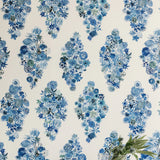 A vase of flowers stands in front of a wall papered in a painterly floral print in shades of blue and navy on a cream field.