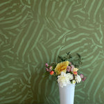 A vase of flowers stands in front of a wall papered in a playful broken stripe print in dark green on a green field.