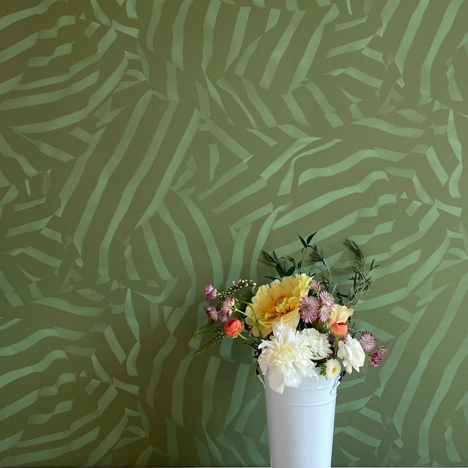 A vase of flowers stands in front of a wall papered in a playful broken stripe print in dark green on a green field.