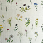 Detail of fabric in a painterly flower print in green and pastels on a cream field.